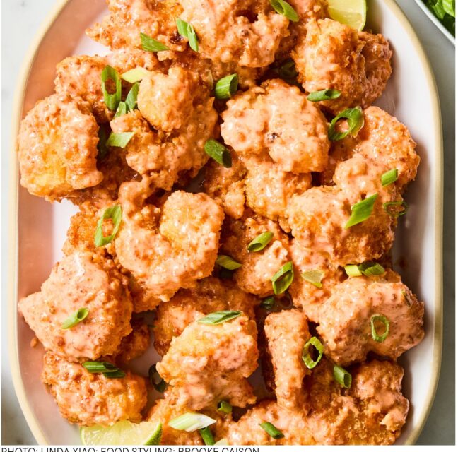Platter of crispy air fryer bang bang shrimp tossed in pink sauce with scallions and lime