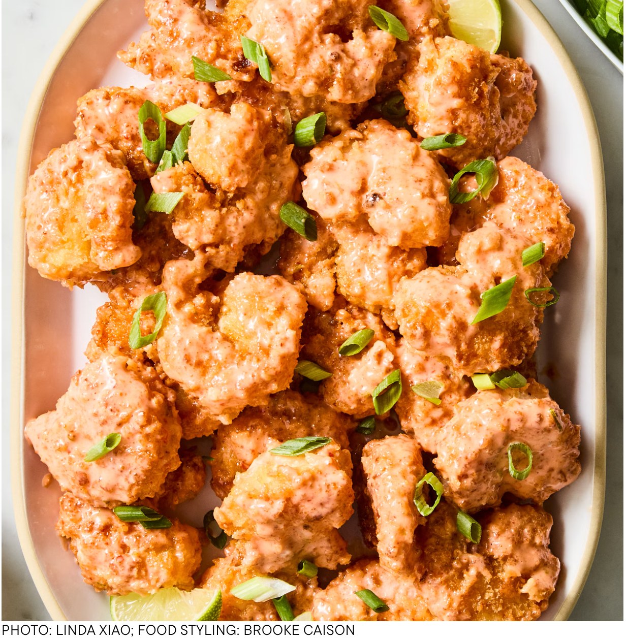 Platter of crispy air fryer bang bang shrimp tossed in pink sauce with scallions and lime