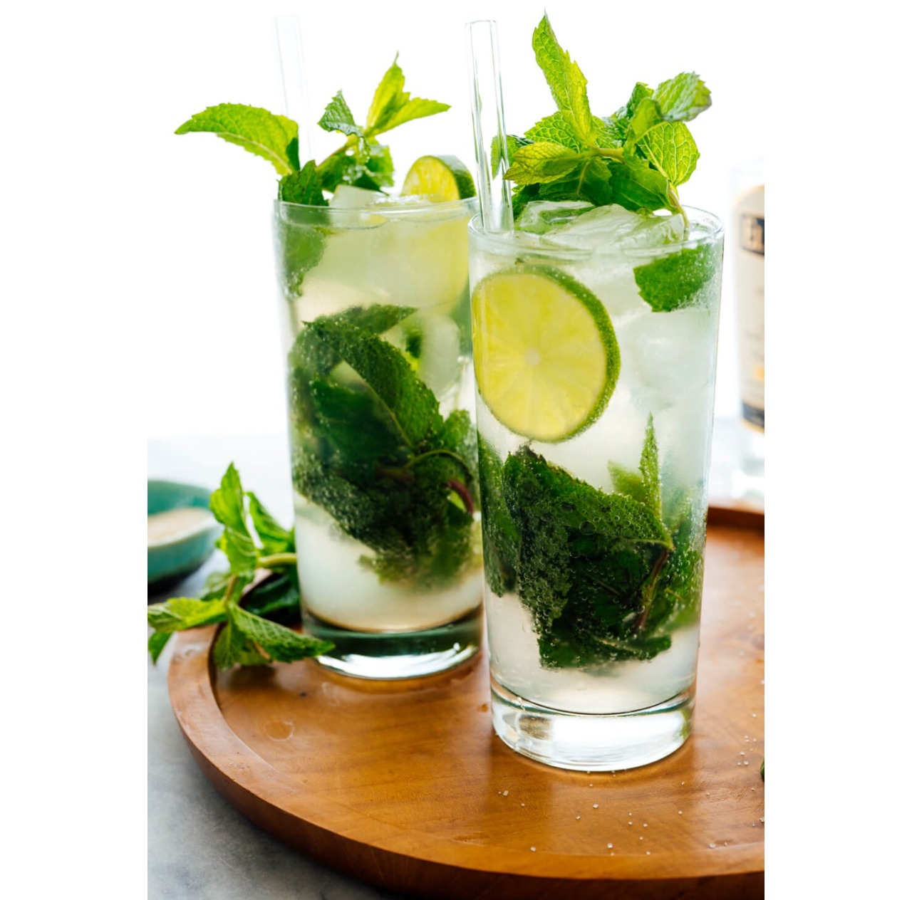 Two tall mojitos with fresh mint, lime wheels and ice on a wooden board