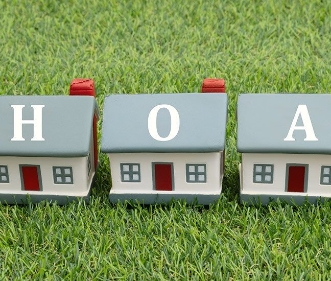 Three toy houses on green grass spelling out the letters HOA