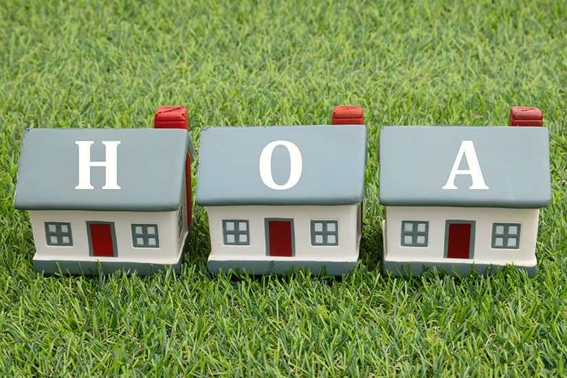 Three toy houses on green grass spelling out the letters HOA