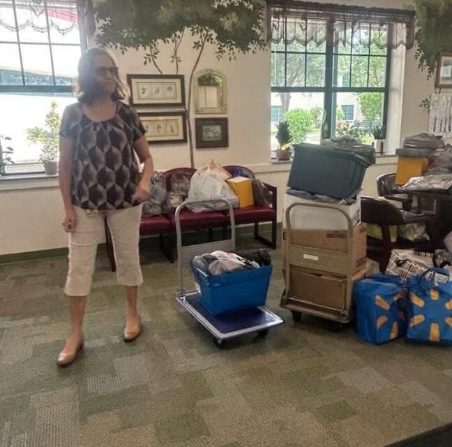 Linda Voto stands beside stacked bins and bags of donated school supplies