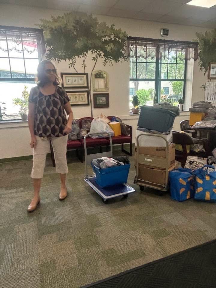 Linda Voto stands beside stacked bins and bags of donated school supplies