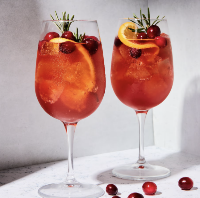 Two glasses of cranberry Aperol spritz with orange slices and rosemary