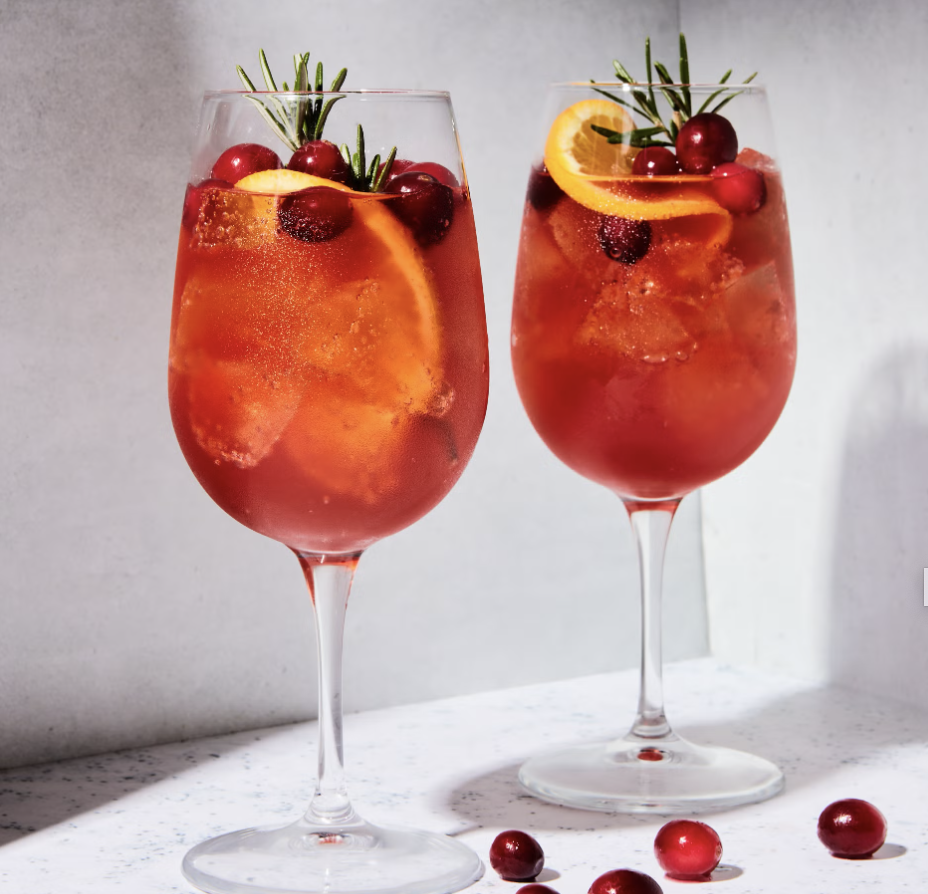 Two glasses of cranberry Aperol spritz with orange slices and rosemary