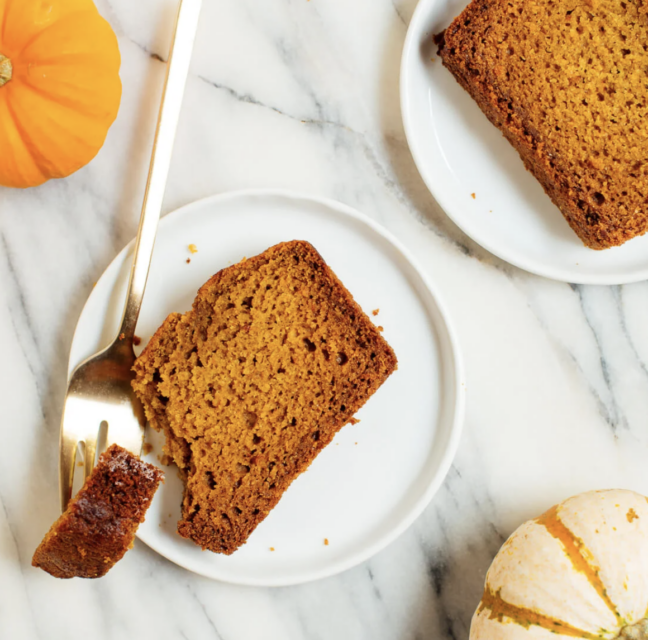 Slices of pumpkin bread on plates with small pumpkins on a marble counter