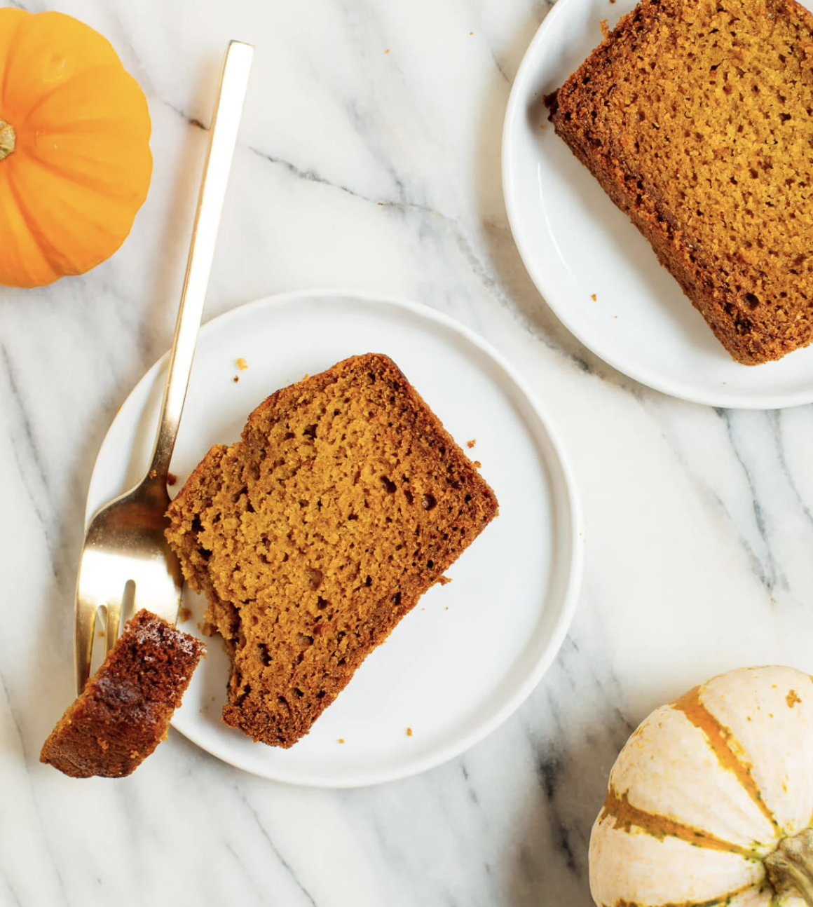 Slices of pumpkin bread on plates with small pumpkins on a marble counter