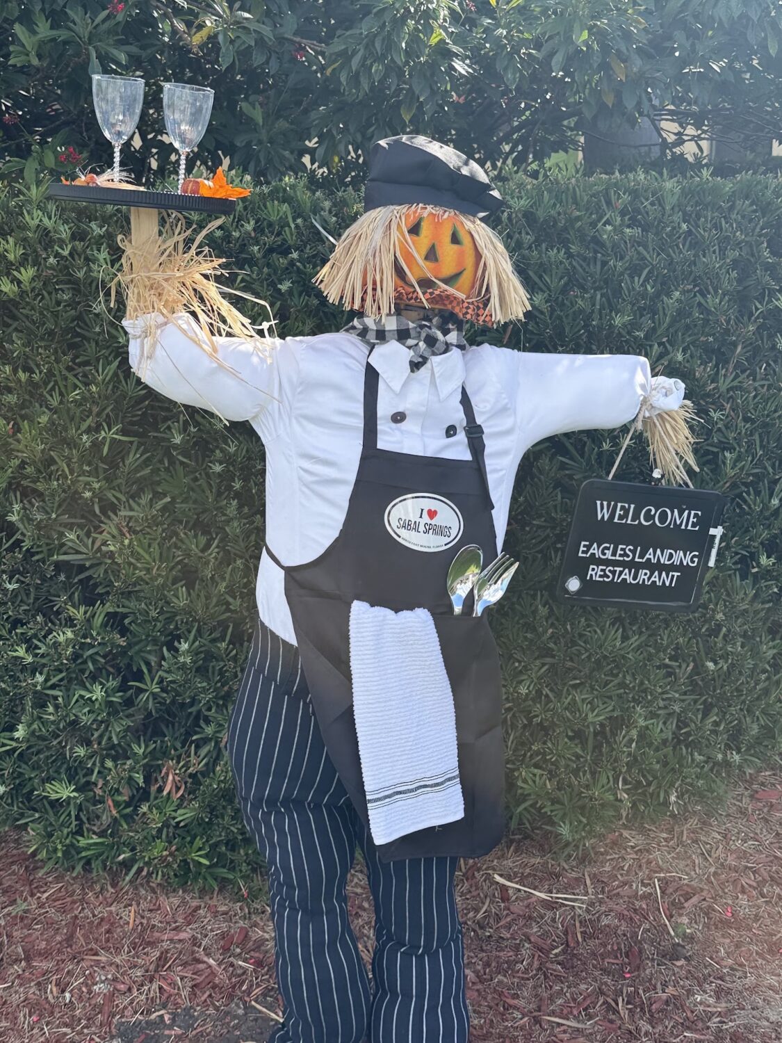 Chef scarecrow with a pumpkin head holding a tray for Eagles Landing Restaurant.