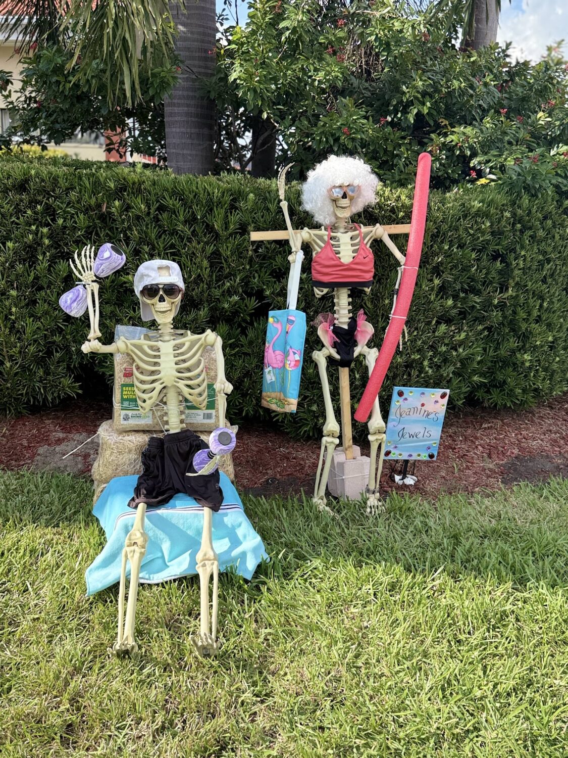 Two skeleton scarecrows posed poolside with floats and towels.