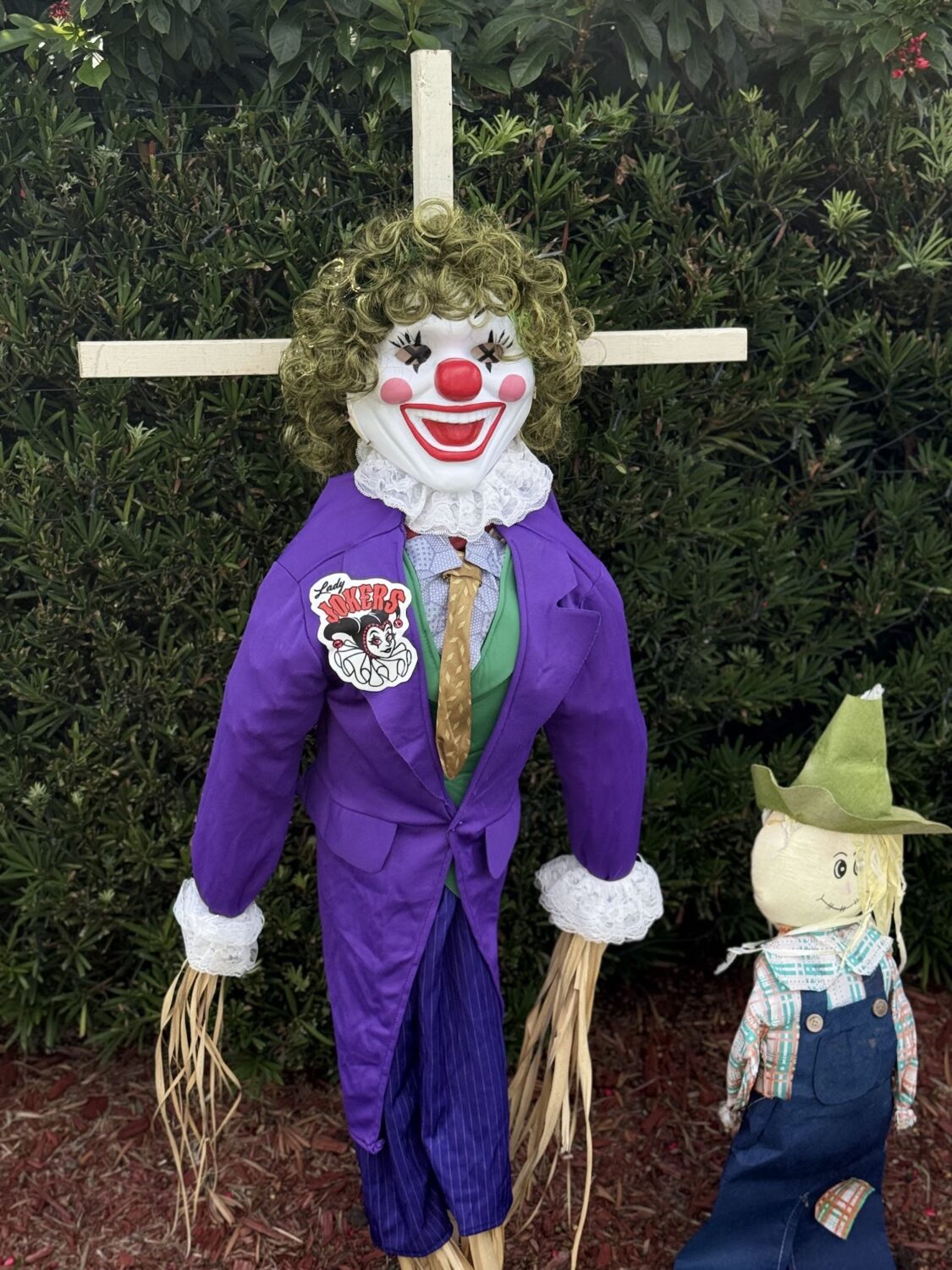 Clown scarecrow in a purple suit beside a small scarecrow.