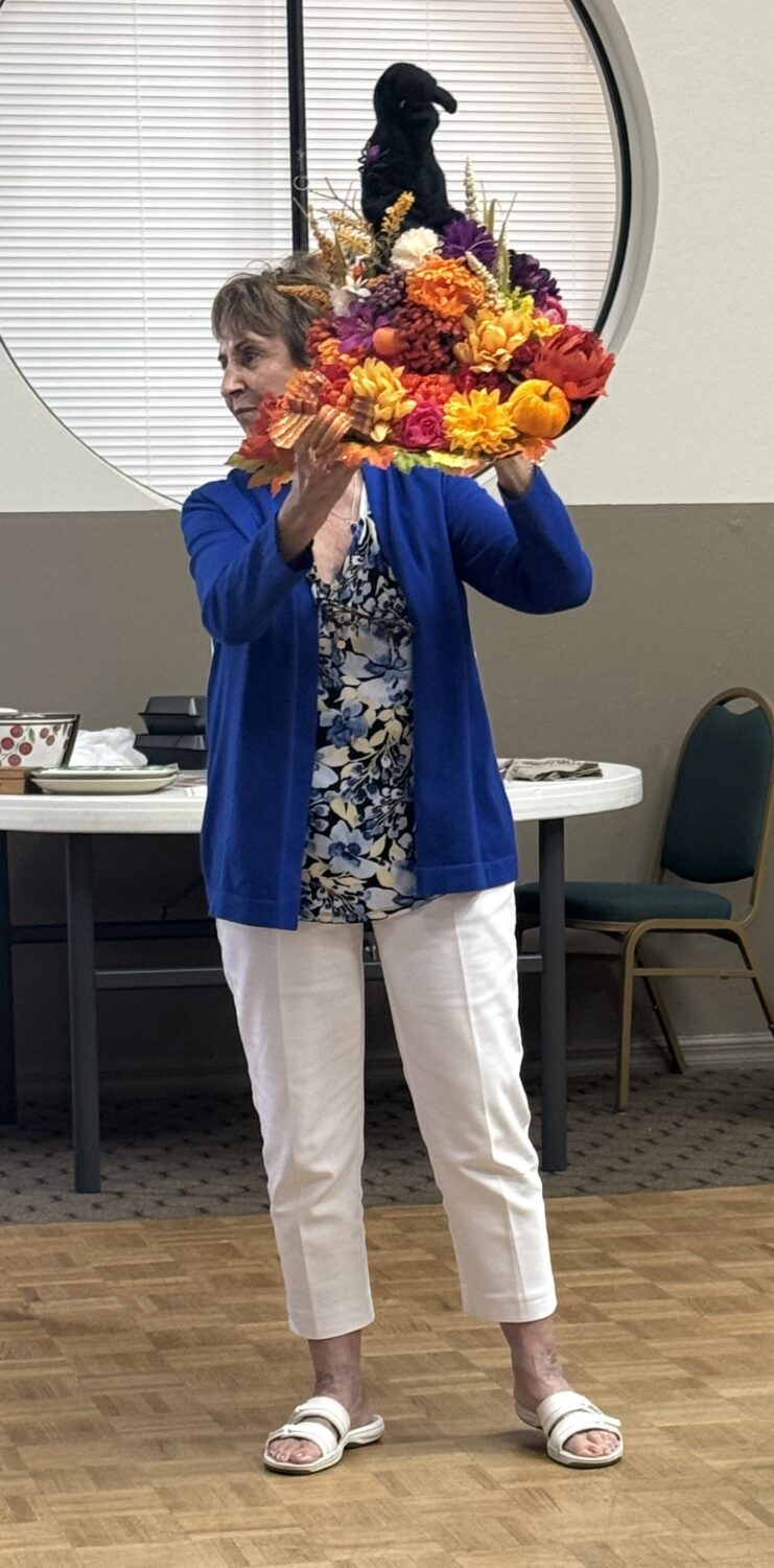 Jan Lambert holding a floral Halloween hat decoration topped with a crow.