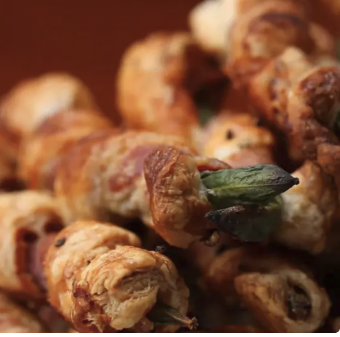 Bacon and puff pastry wrapped green bean twists on a platter.