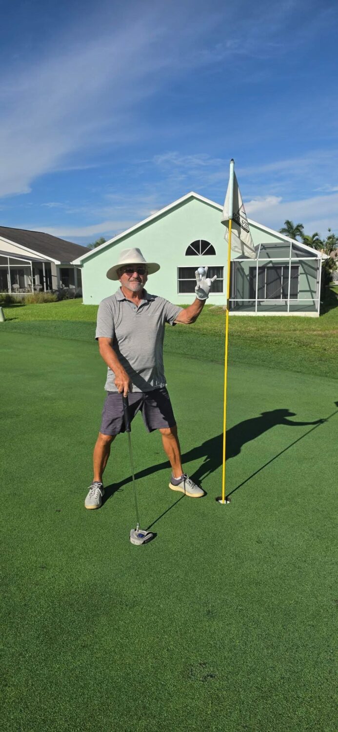 Carter Johnson holding a club beside the flagstick on the sixth green.