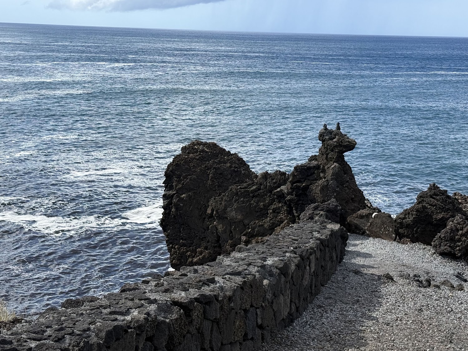 Lava rock formations meeting the ocean along a coastal path.