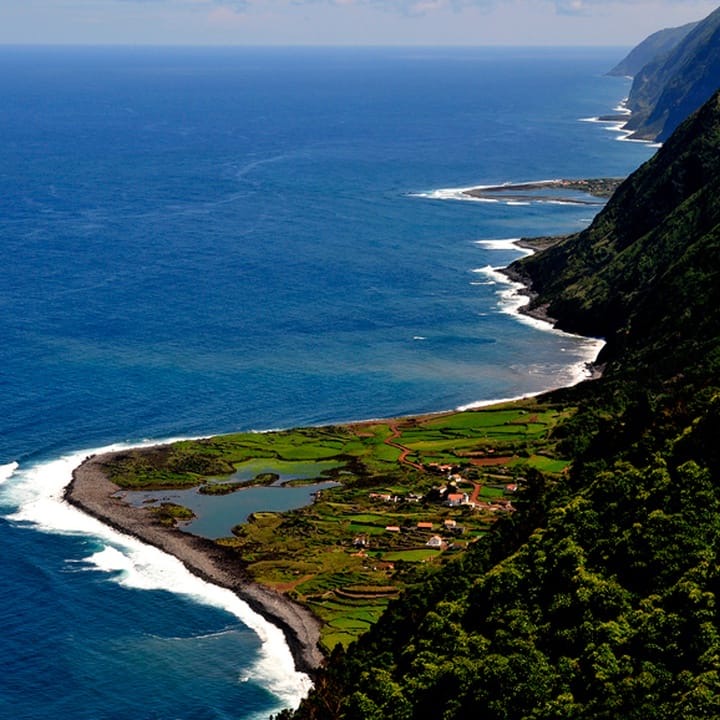 Aerial view of a green coastal faja beside the blue Atlantic.